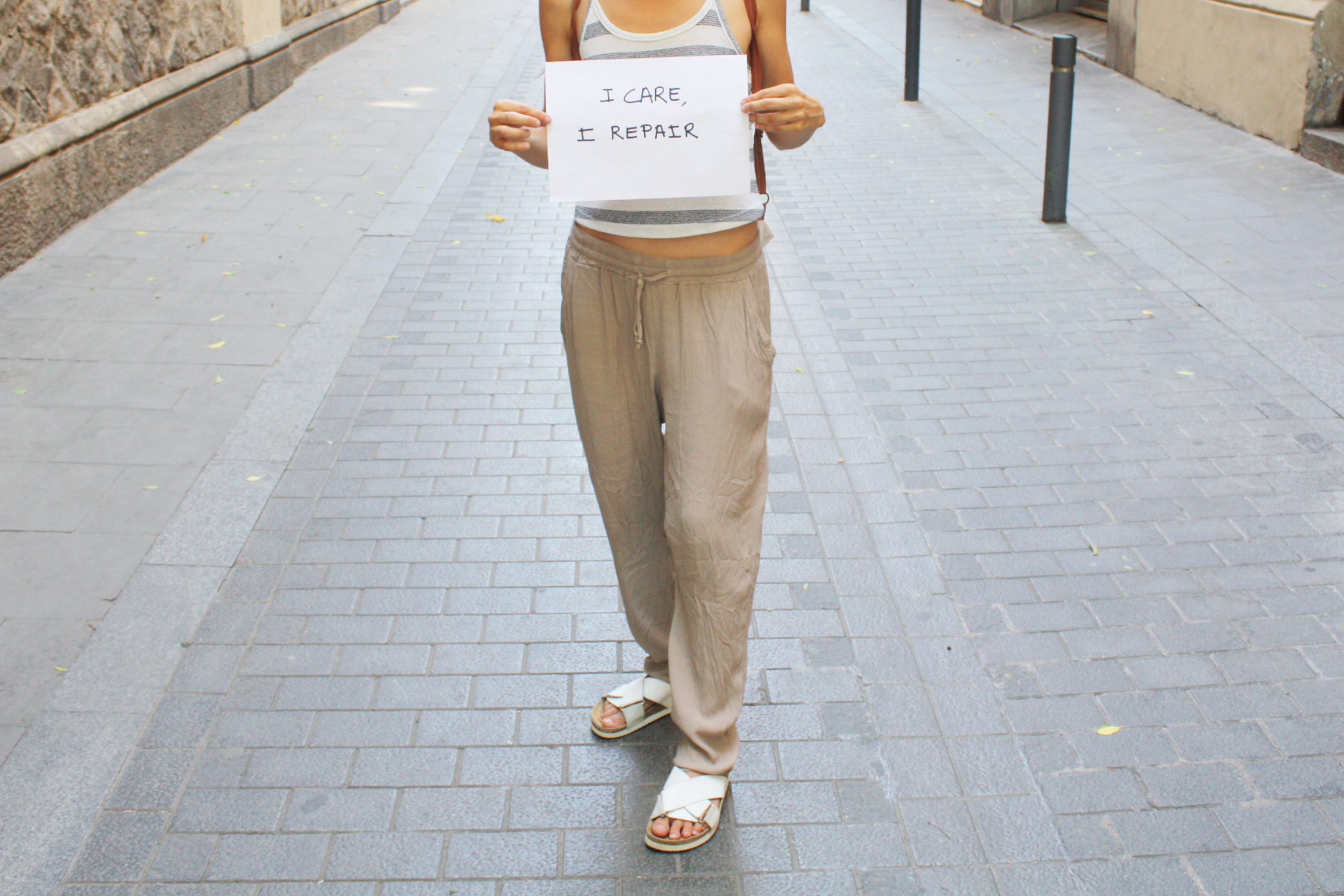 Chica vistiendo sandalias de piel renovadas con los productos TRG the One y mostrando un cartel que pone "I Care, I Repair"